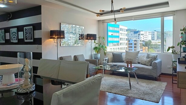 Un salon moderne avec un canapé, une table basse et des objets de décoration. Une grande fenêtre offre une vue sur la ville.