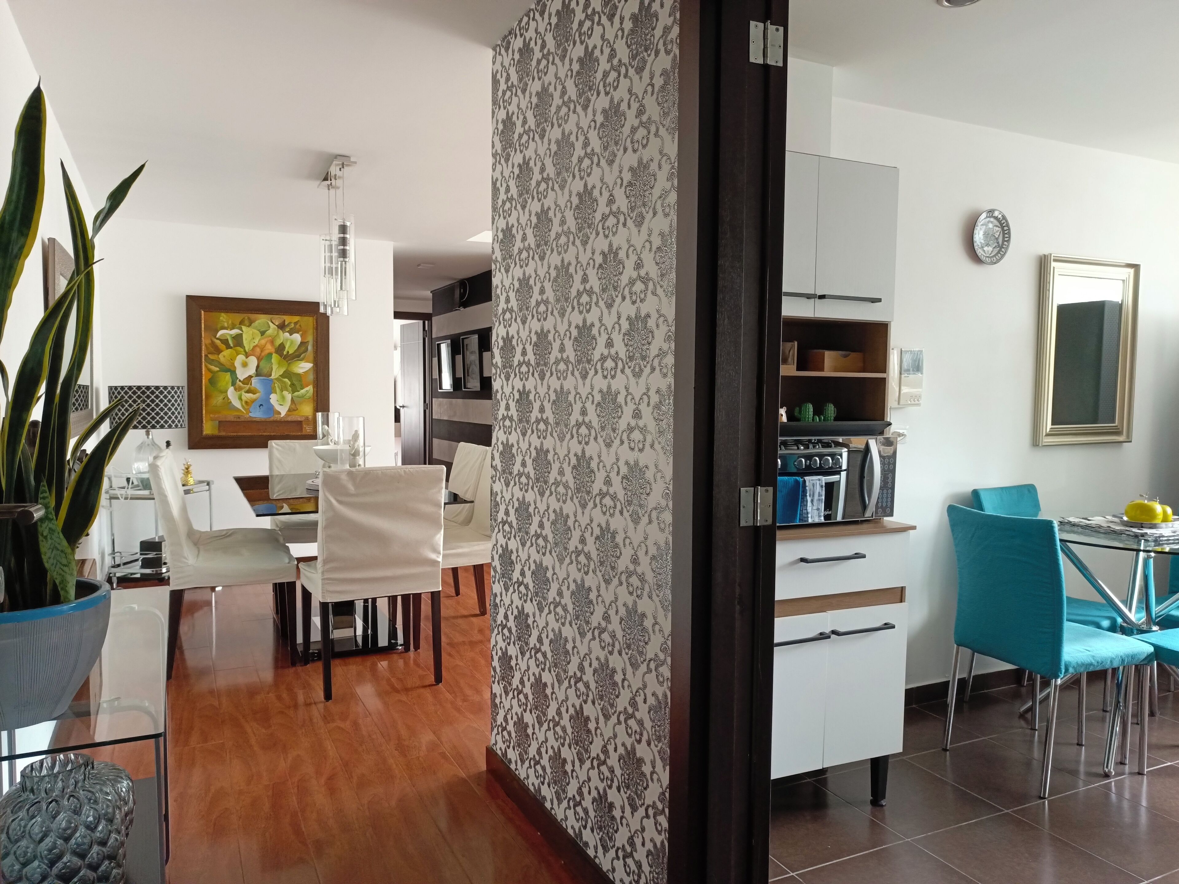 A modern kitchen with white cabinets, a stove, and a microwave. There is a dining area with a table and chairs, and a potted plant.