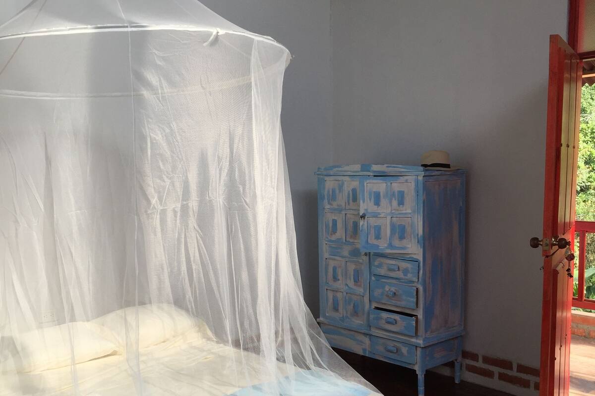 A bed with a white mosquito net, a blue chest of drawers, and a wooden floor.