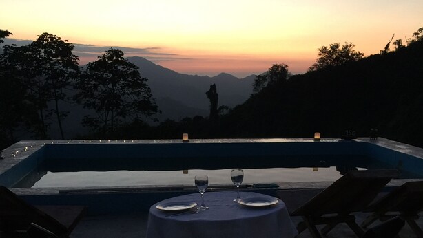 A sunset view from a poolside table with two chairs, a table set with plates and glasses, and a candle on the table. - Finca Cafetera San Rafael (Santa Marta)