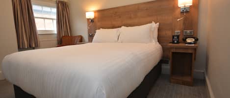 A hotel room with a large bed, wooden headboard, two bedside lamps, a nightstand with a telephone, and a window with curtains.