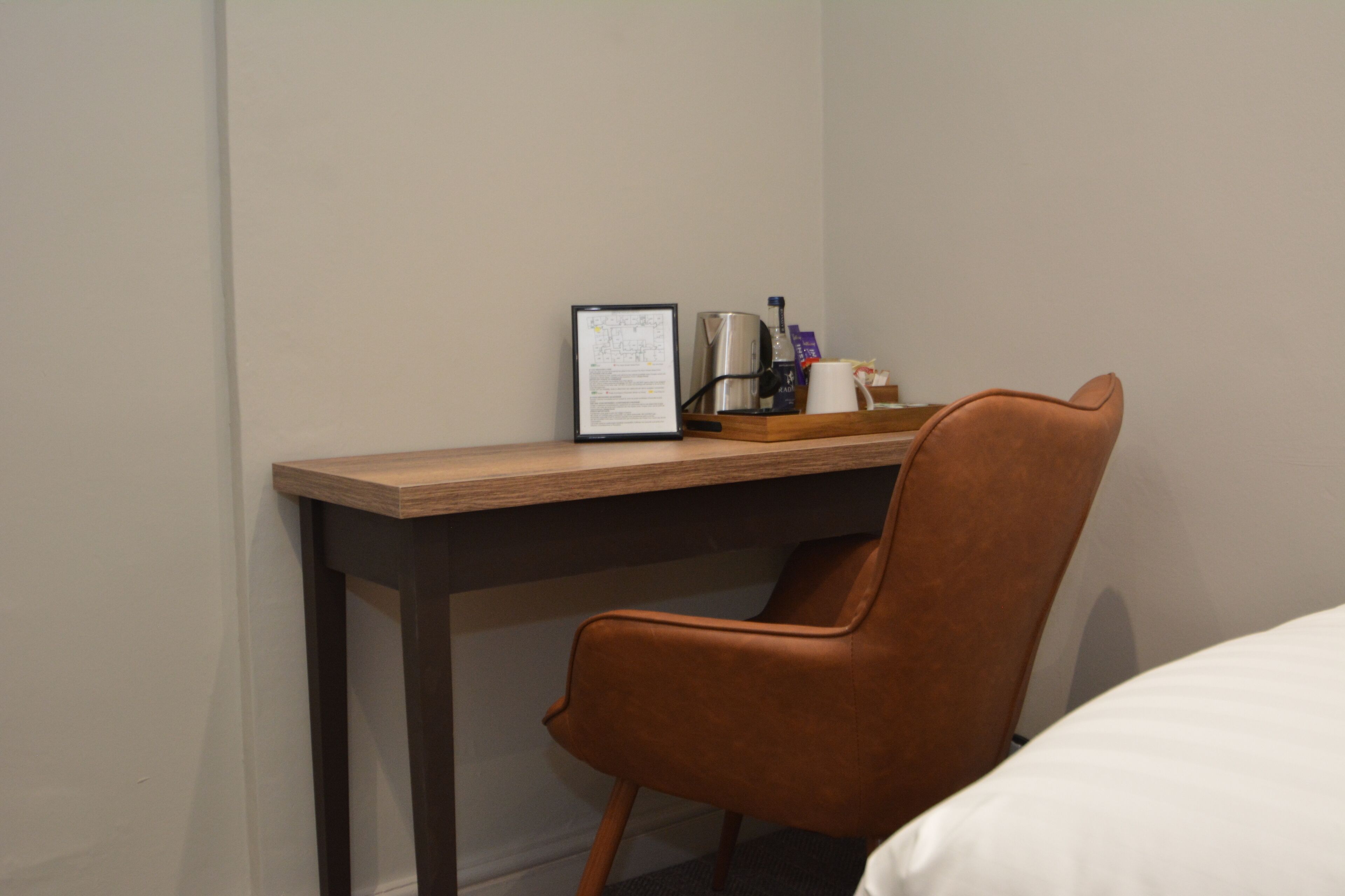 Une chambre d’hôtel avec un bureau en bois, un fauteuil en cuir marron, un document encadré, une machine à café et une tasse.