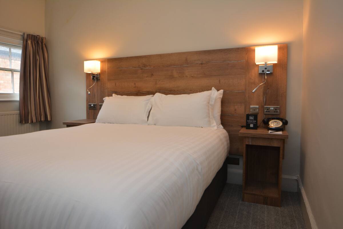 A neatly made bed with white linens, two bedside lamps, and a wooden headboard.