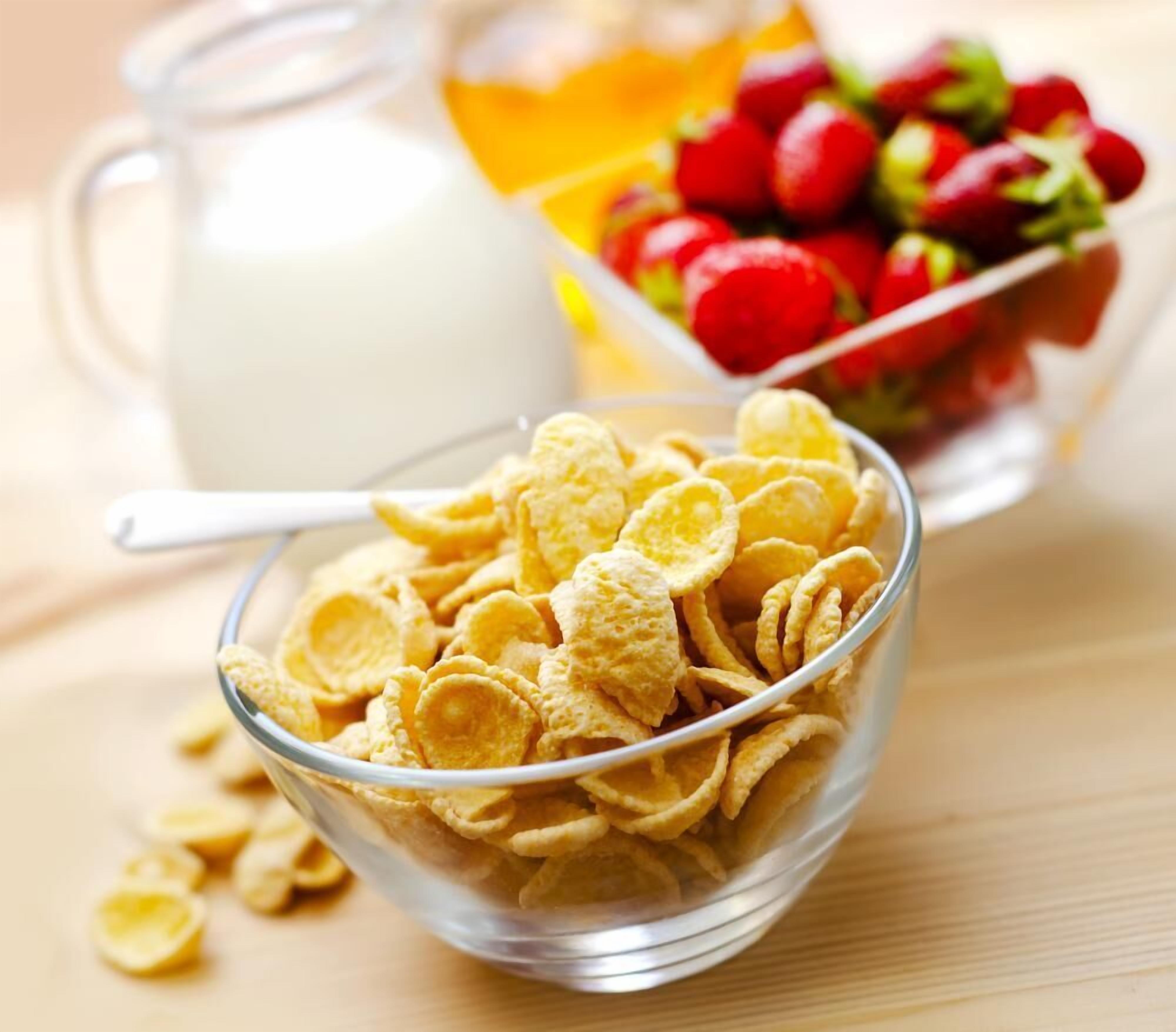 A bowl of cereal, a jug of milk, and a bowl of fruit on a wooden table.