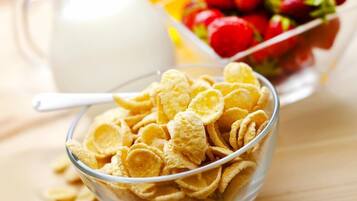 A bowl of cereal, a jug of milk, and a bowl of fruit on a wooden table.