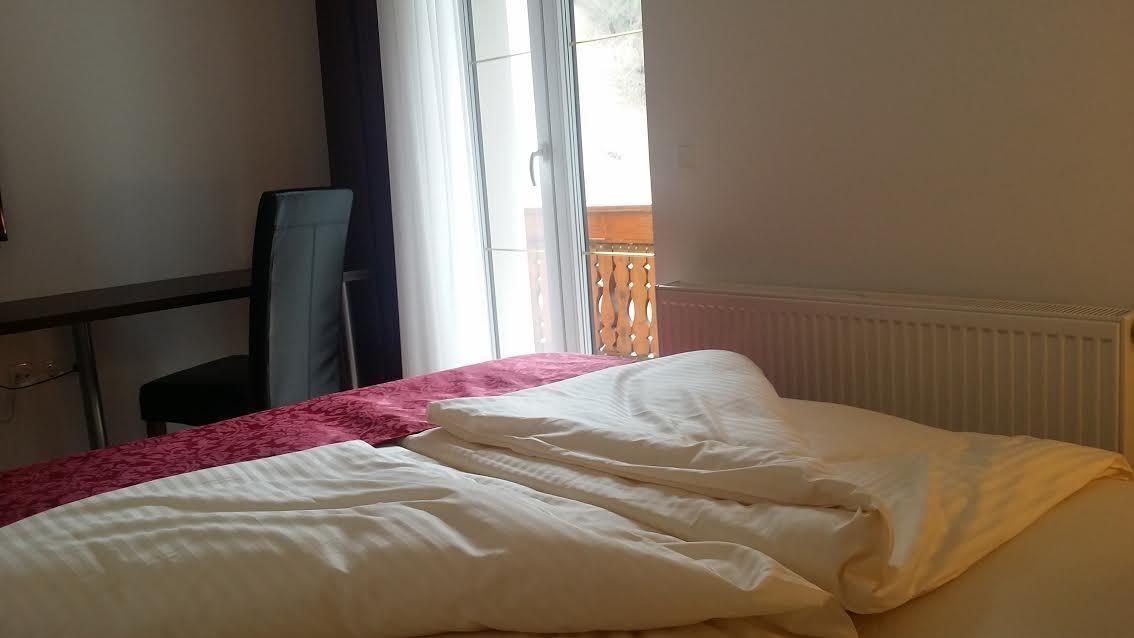 Un dormitorio con cama, una silla y un ventanal con cortinas.