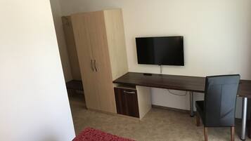 A small room with a wooden desk, a black TV, a red patterned rug, and a wardrobe.