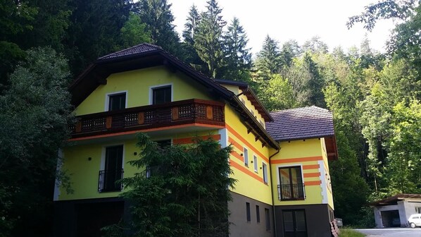 Una casa de dos pisos con balcón, rodeada de bosque denso.