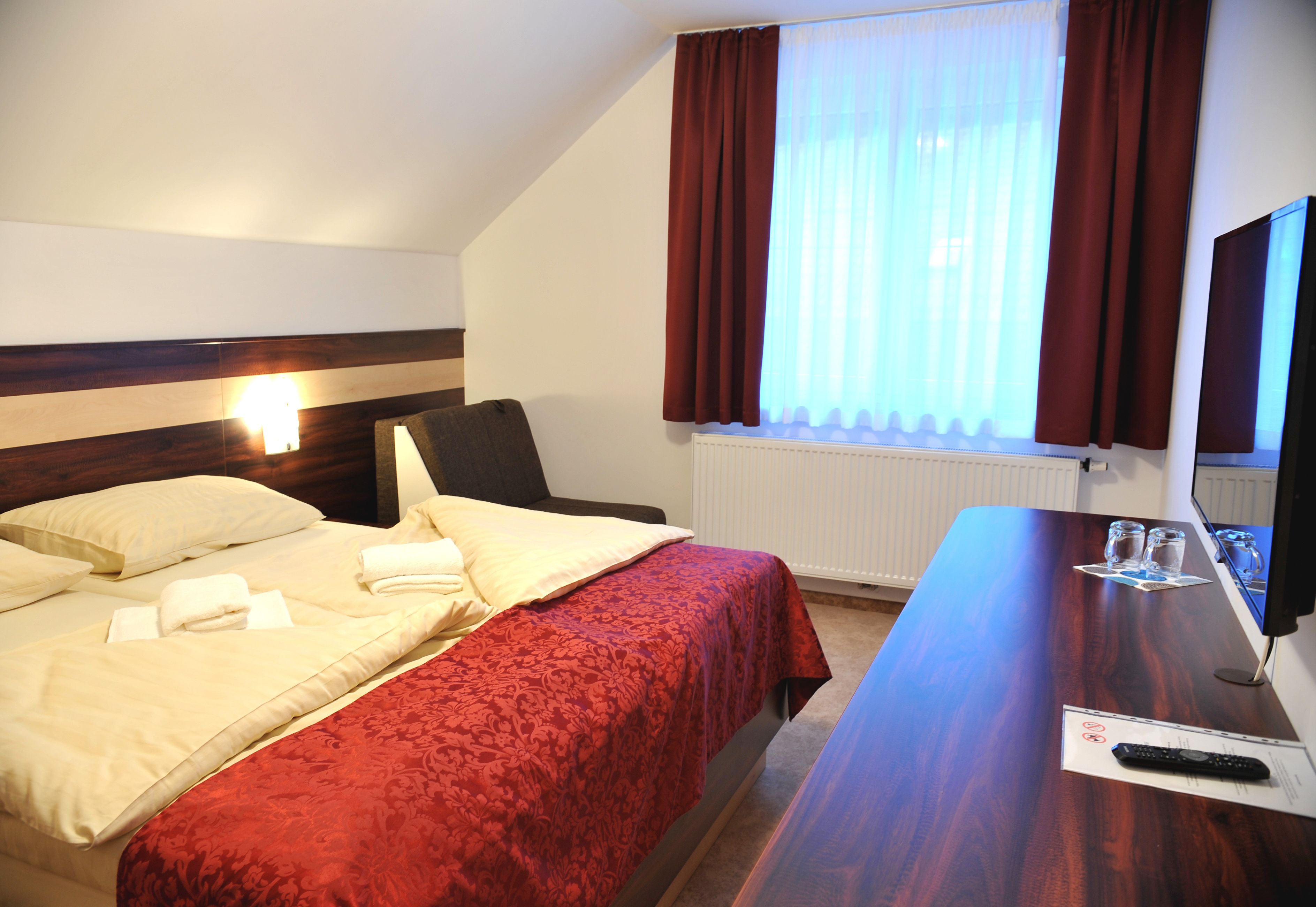 A hotel room with a bed, a desk, a chair, a TV, and a window with curtains.