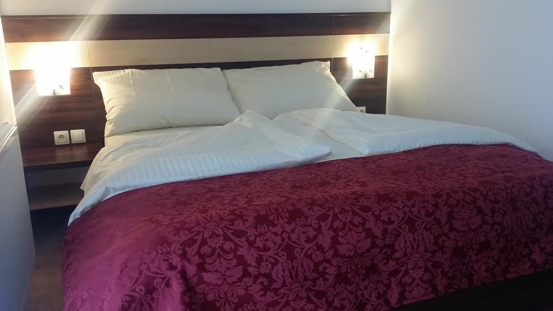A neatly made bed with white linens and a red patterned bedspread, a wooden headboard, and two wall-mounted lights.