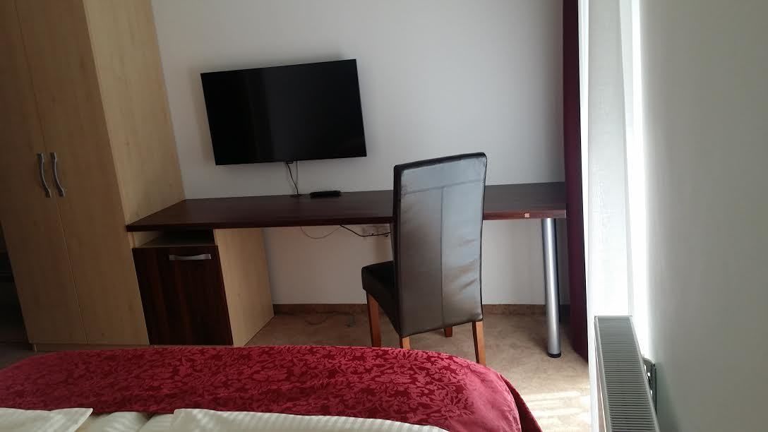 Habitación de hotel con cama, escritorio, silla, televisor y radiador.