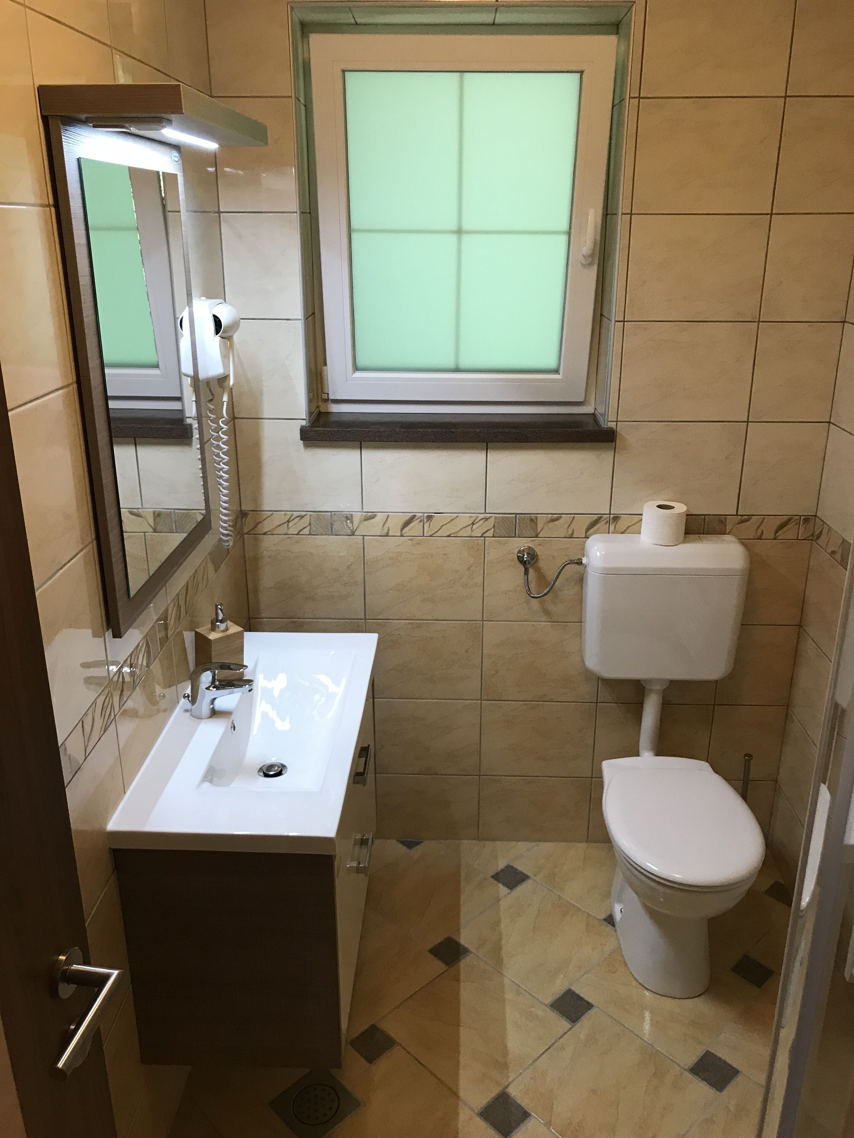 Un baño con lavamanos blanco, inodoro y ventana sobre el inodoro.