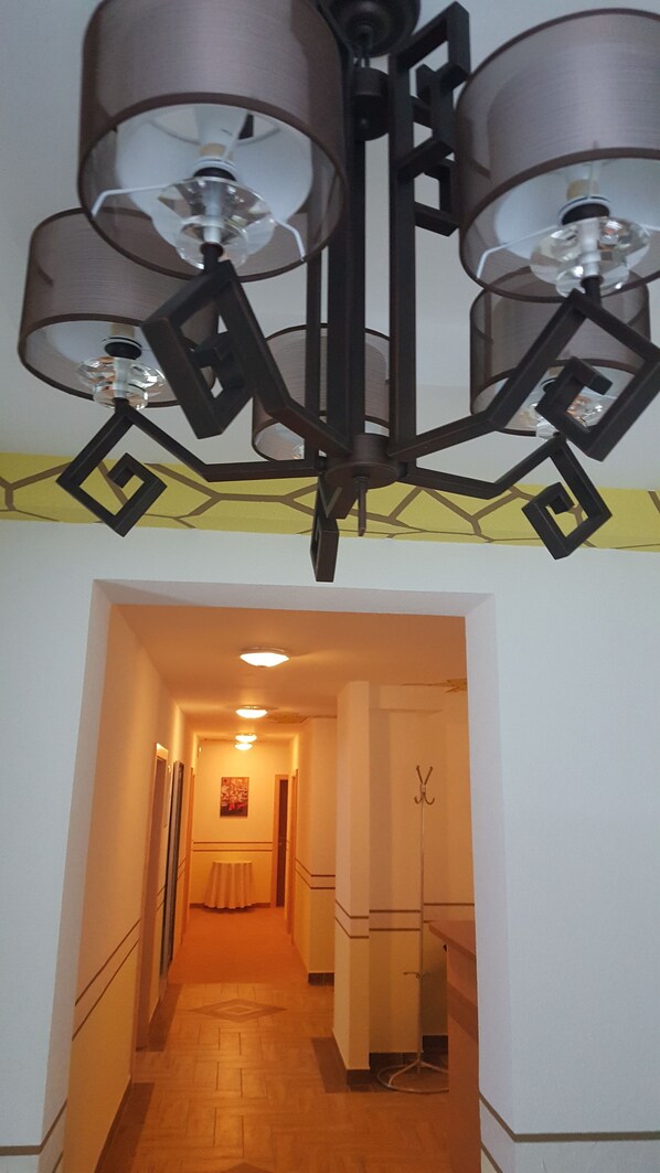 Un pasillo con una lámpara de araña moderna, un perchero y una puerta que da a otra habitación.