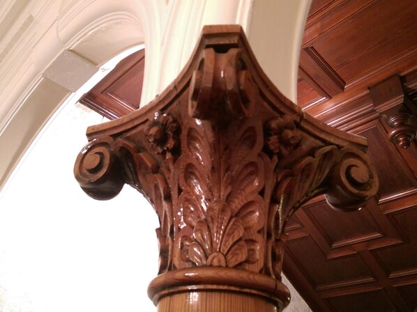 Detalle arquitectónico de madera con motivos florales tallados y una base redondeada, probablemente parte de la estructura interior de un edificio.