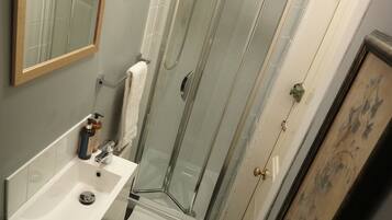 A bathroom with a glass-enclosed shower, a sink with a mirror, and toiletries on the counter.