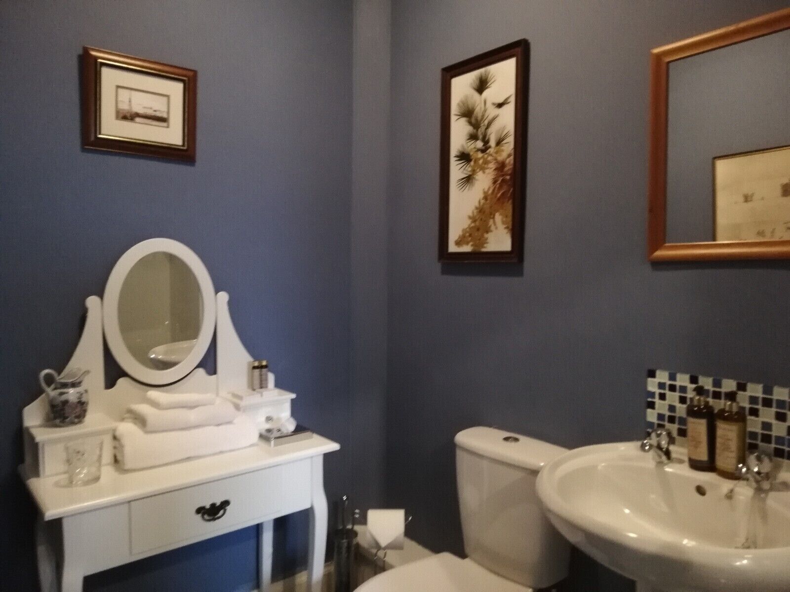 Une salle de bain avec un meuble-lavabo blanc, un grand miroir, des toilettes et un lavabo avec un pare-éclaboussures carrelé.