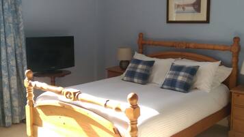 A neatly made bed with a wooden headboard, a television on a stand, and a lamp on a bedside table.