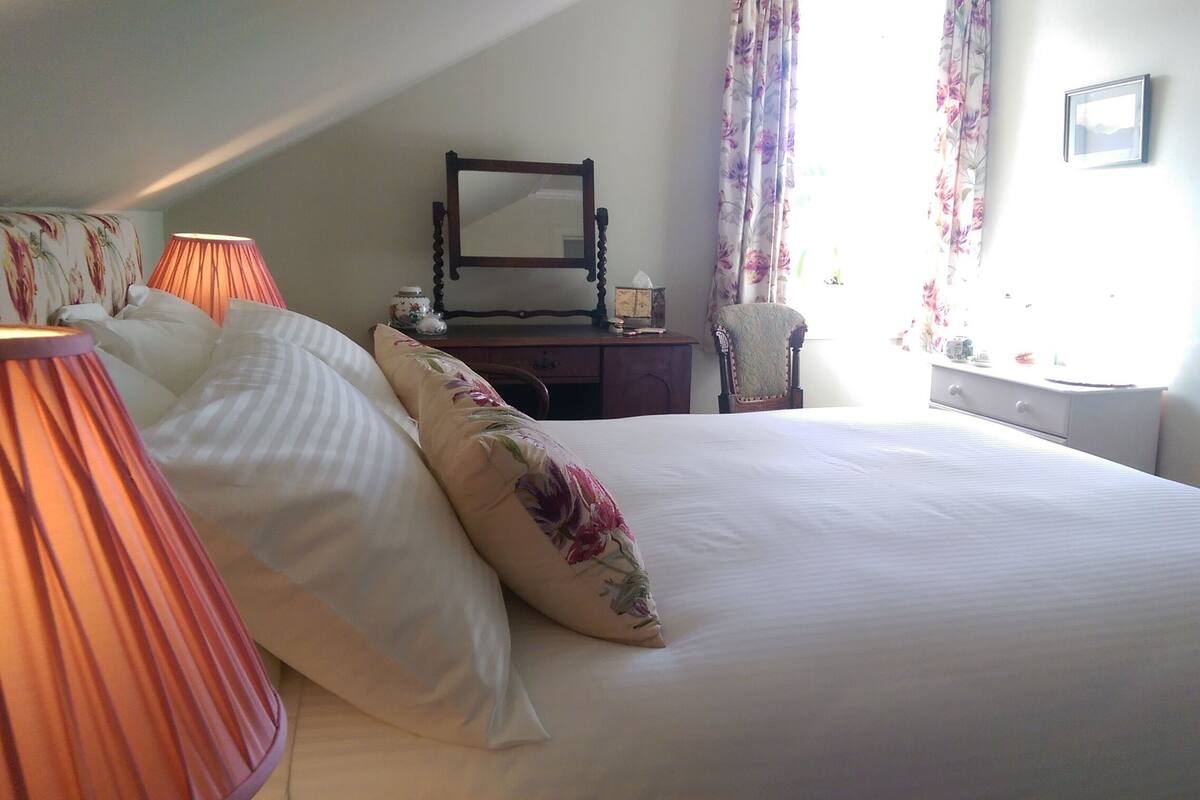 A bedroom with a bed, a nightstand, a dresser, a mirror, and a window with curtains.