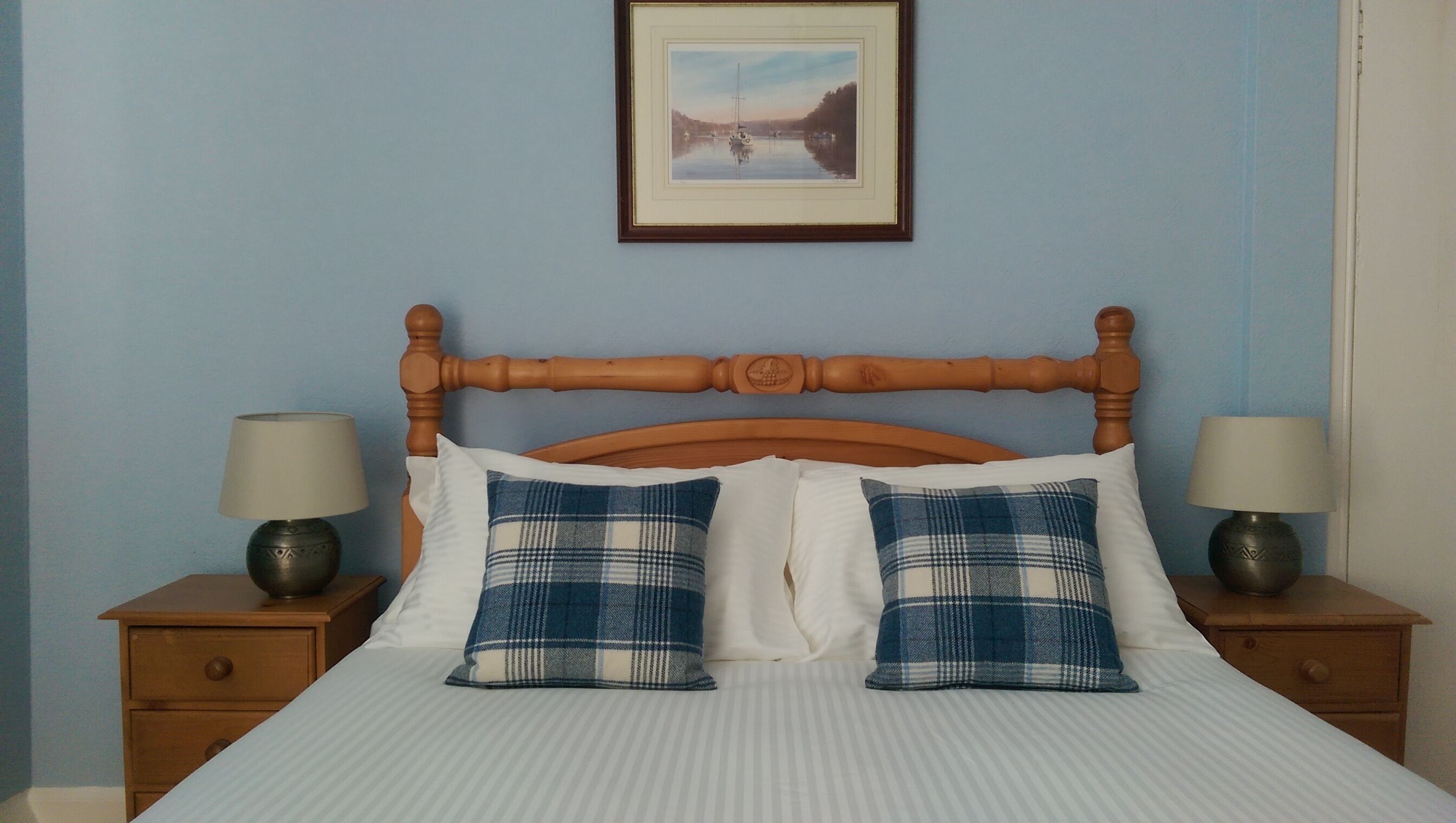 Un letto con testiera in legno, due comodini con lampade e un quadro appeso alla parete.