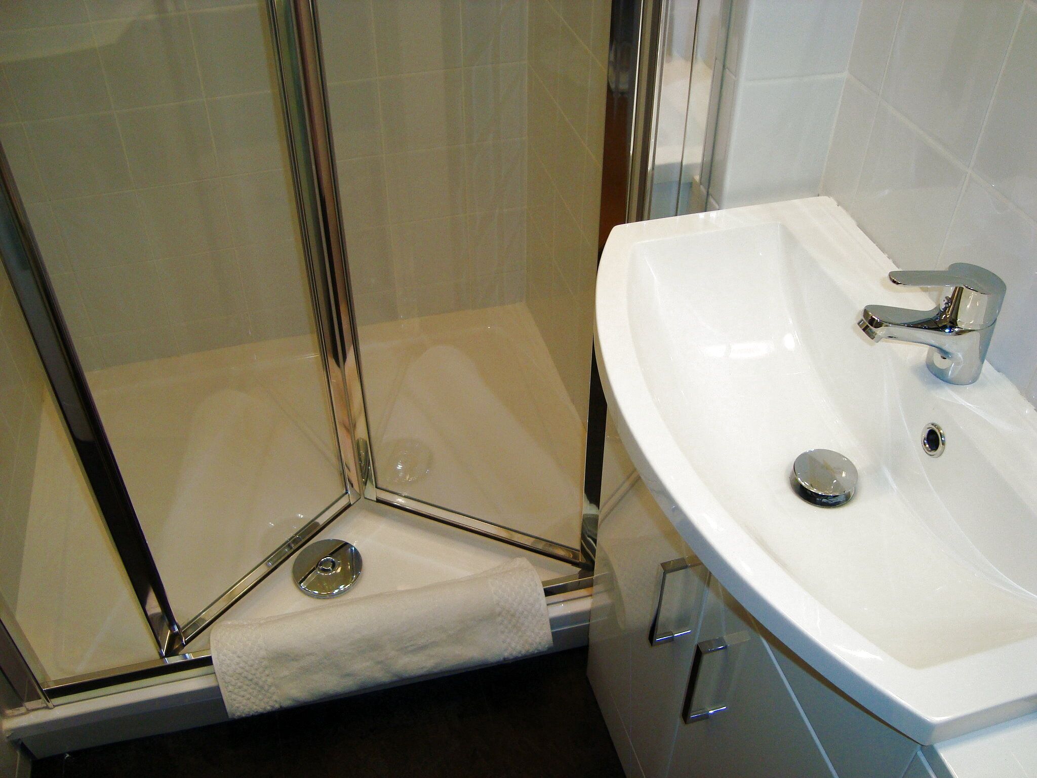 Une salle de bain avec une douche à parois de verre, un lavabo blanc et un porte-serviettes.
