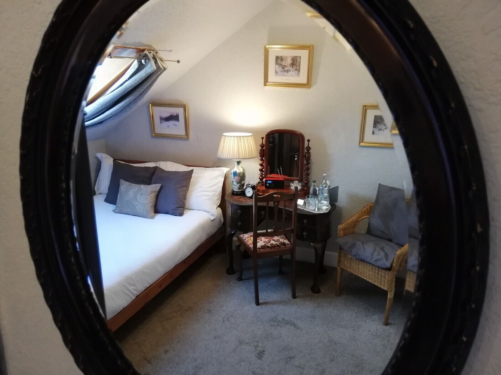 A bedroom with a bed, a chair, a desk with a lamp, and a mirror.