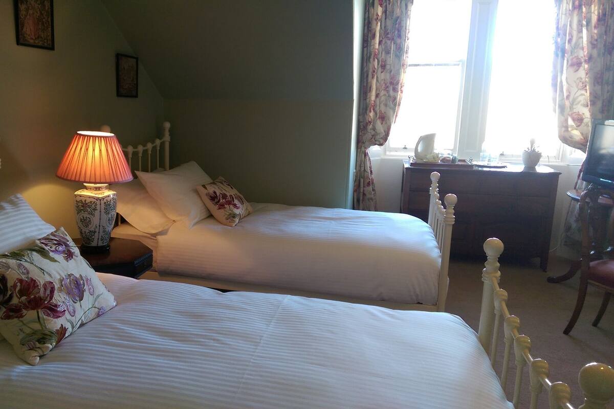 A twin room with two beds, a bedside table with a lamp, a desk, and a chair.