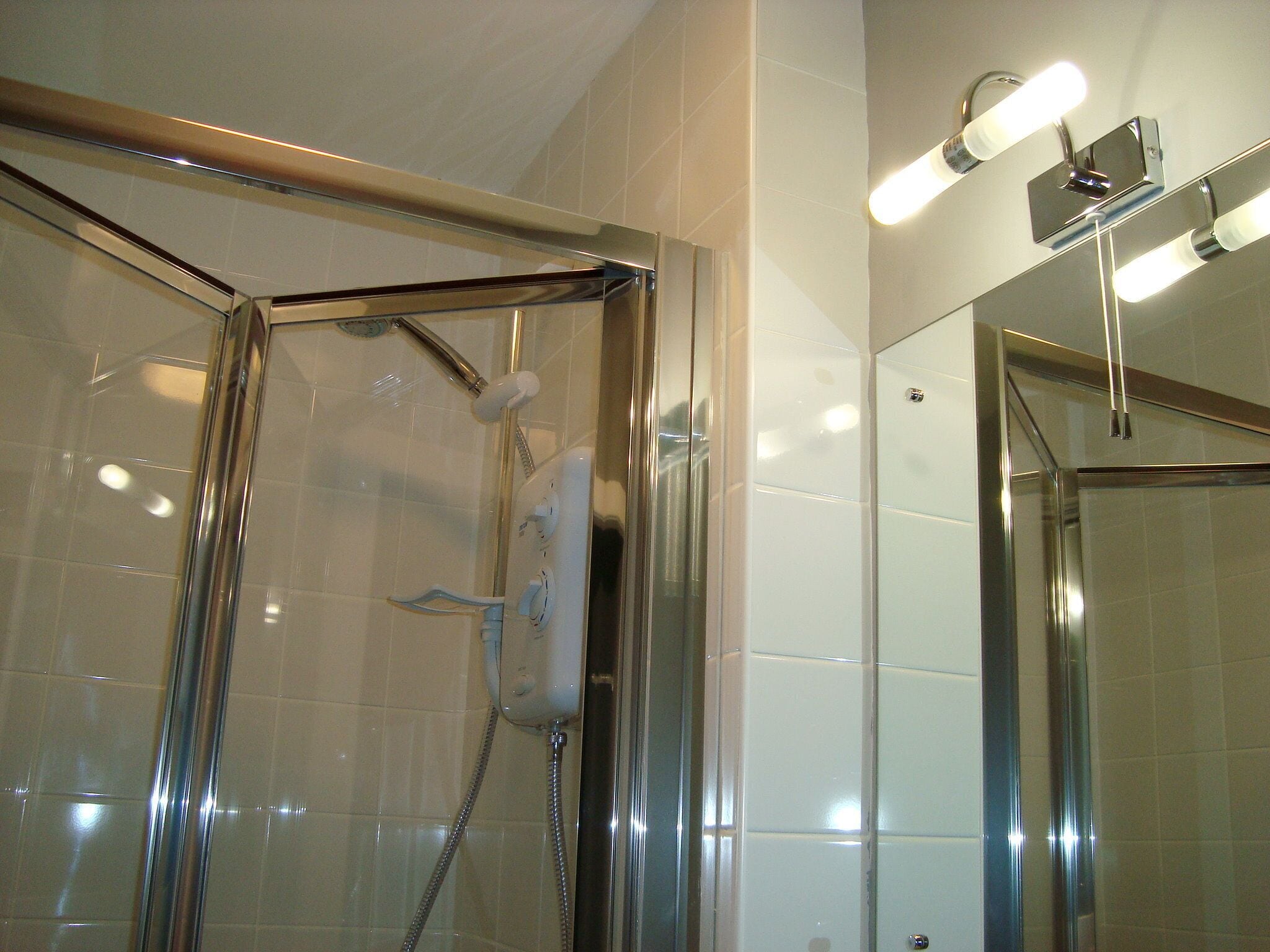 Una ducha con cerramiento de vidrio, accesorios cromados y un aplique de pared.