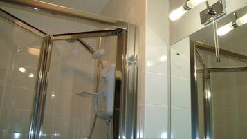 Una ducha con cerramiento de vidrio, accesorios cromados y un aplique de pared.
