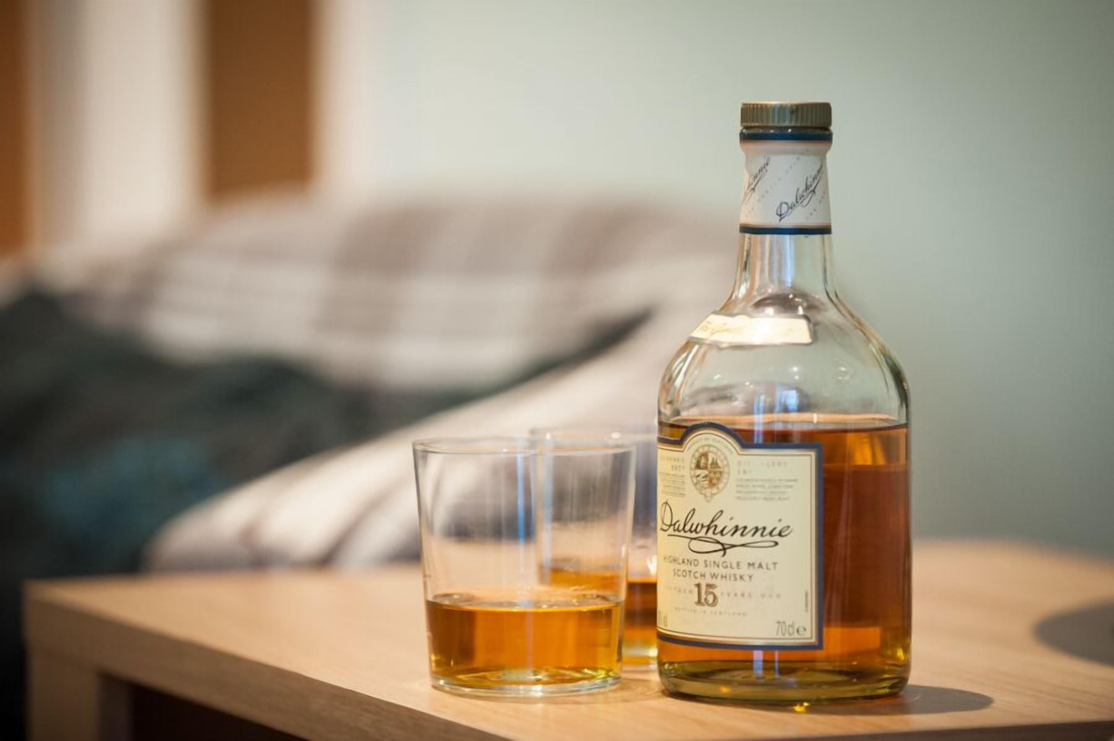 A bottle of Dalwhinie single malt scotch whisky and a glass on a wooden surface with a blurred background.