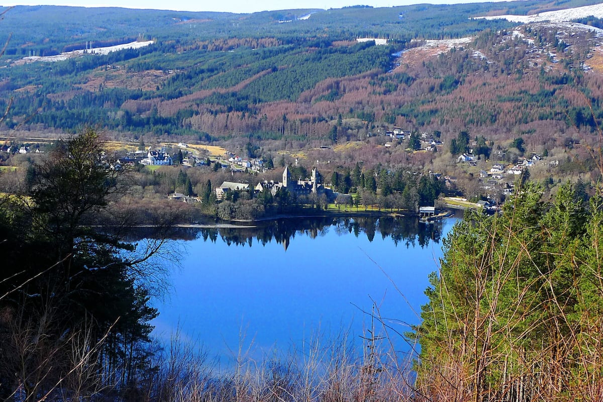 Ein See, umgeben von bewaldeten Hügeln, mit einem kleinen Dorf und einer Kirche.