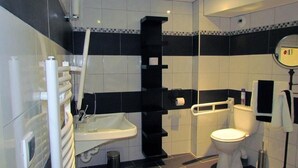 A modern bathroom with a white sink, black and white tiled walls, a black towel rack, and a white toilet. - Hôtel de France et de Russie (Thiviers)