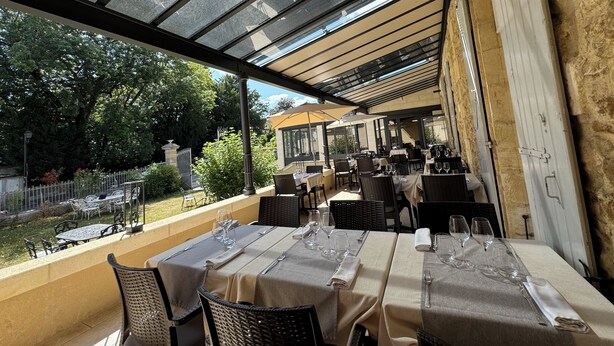 An outdoor restaurant with tables set for dining, a glass roof, and a view of the garden. - Hôtel de France et de Russie (Thiviers)