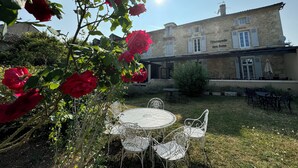 A stone building with a sign reading "L'Escapade des Sens" and a garden with white metal chairs and tables. - Hôtel de France et de Russie (Thiviers)
