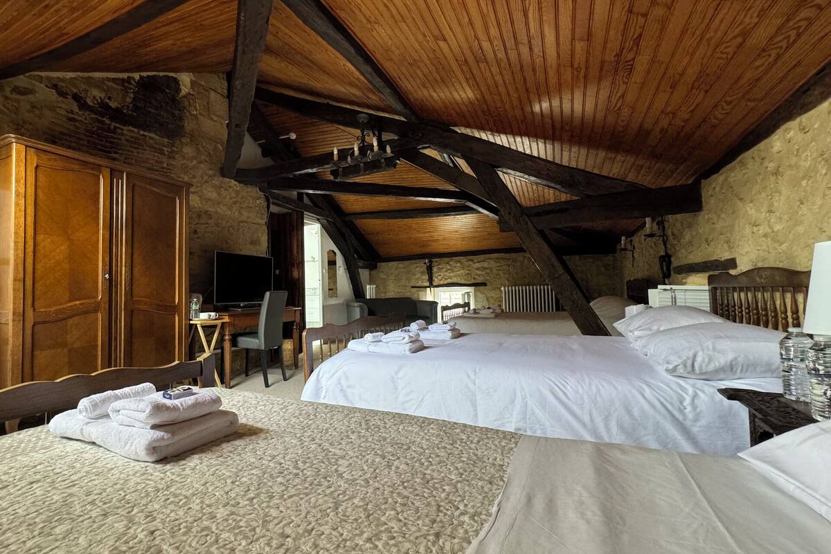 A bedroom with two beds, a wooden ceiling, a stone wall, and a wooden wardrobe.