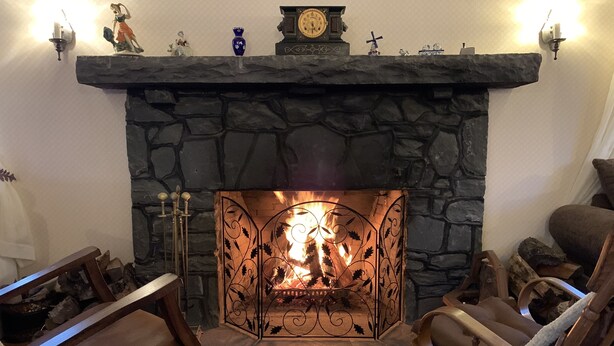 A stone fireplace with a fire, flanked by two wooden armchairs and a patterned rug. - Georgian Garden Inn (Windham)