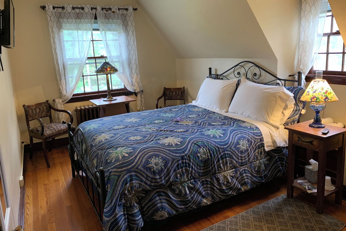 A bedroom with a large bed, a chair, a table with a lamp, and a window with curtains.