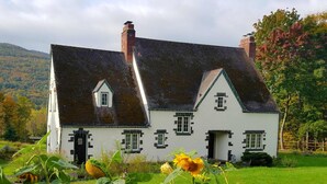 A traditional white house with a steeply pitched roof, multiple chimneys, and a well-maintained garden with sunflowers. - Georgian Garden Inn (Windham)