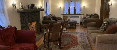 A cozy living room with a stone fireplace, wooden flooring, and a mix of sofas and chairs.
