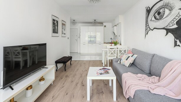 A modern living room with a flat-screen TV, a grey sofa, a white coffee table, and a kitchen in the background. - ShortStayPoland Aleje Jerozolimskie B13 (Warsaw)