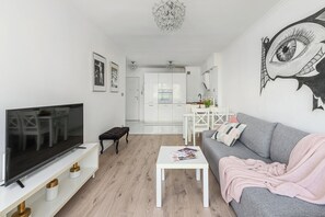 Una sala de estar moderna con una televisión de pantalla plana, un sofá gris, una mesa de centro blanca y una cocina al fondo.