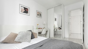 A modern bedroom with a bed, bedside table, desk, chair, and a wardrobe. - ShortStayPoland Aleje Jerozolimskie B13 (Warsaw)