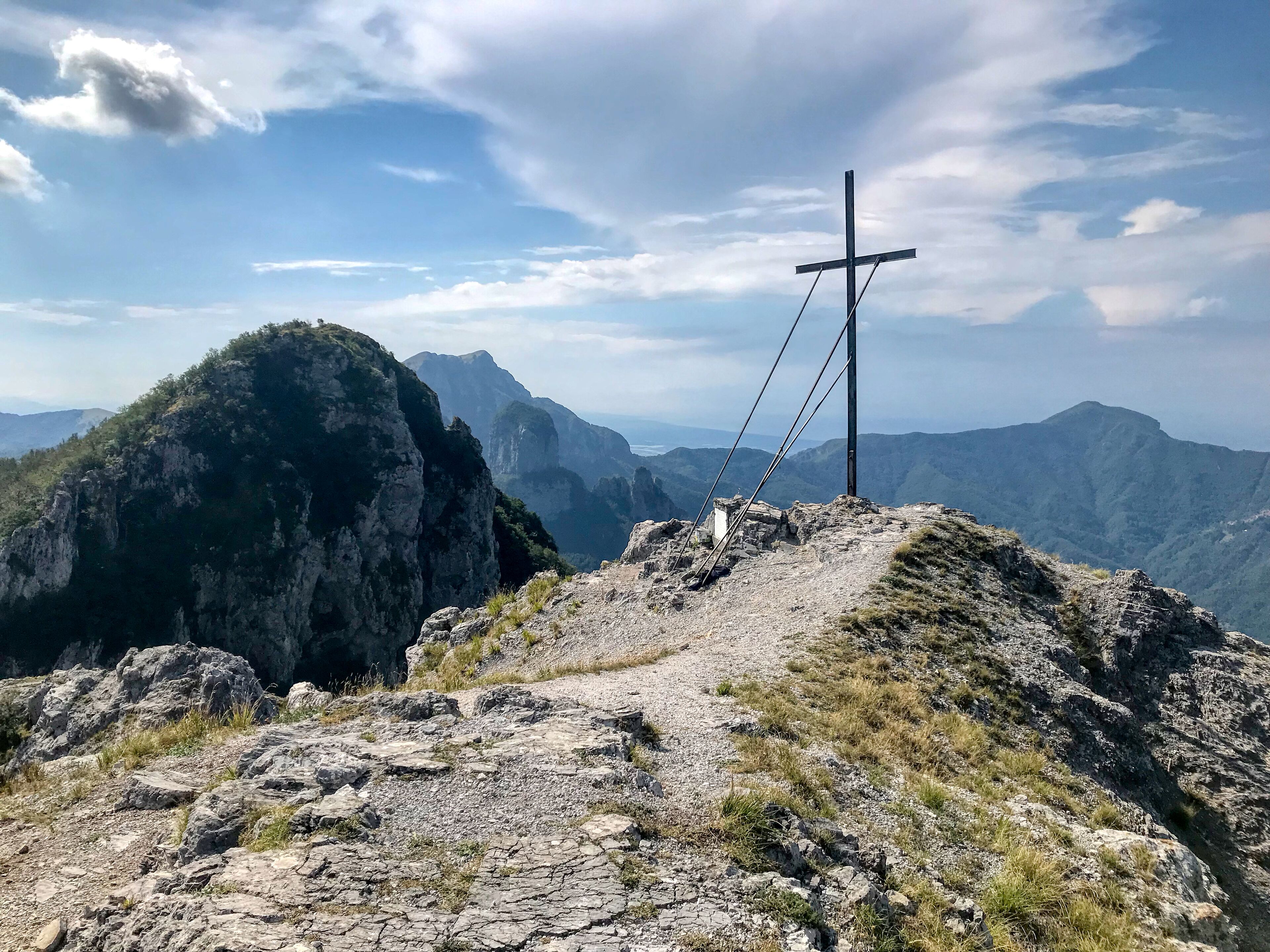 Une croix au sommet d’une montagne, avec un ciel dégagé et des montagnes à l’horizon.