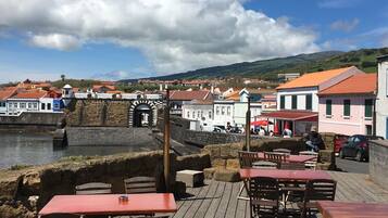 A waterfront dining area with tables and chairs, a stone wall, and buildings in the background.