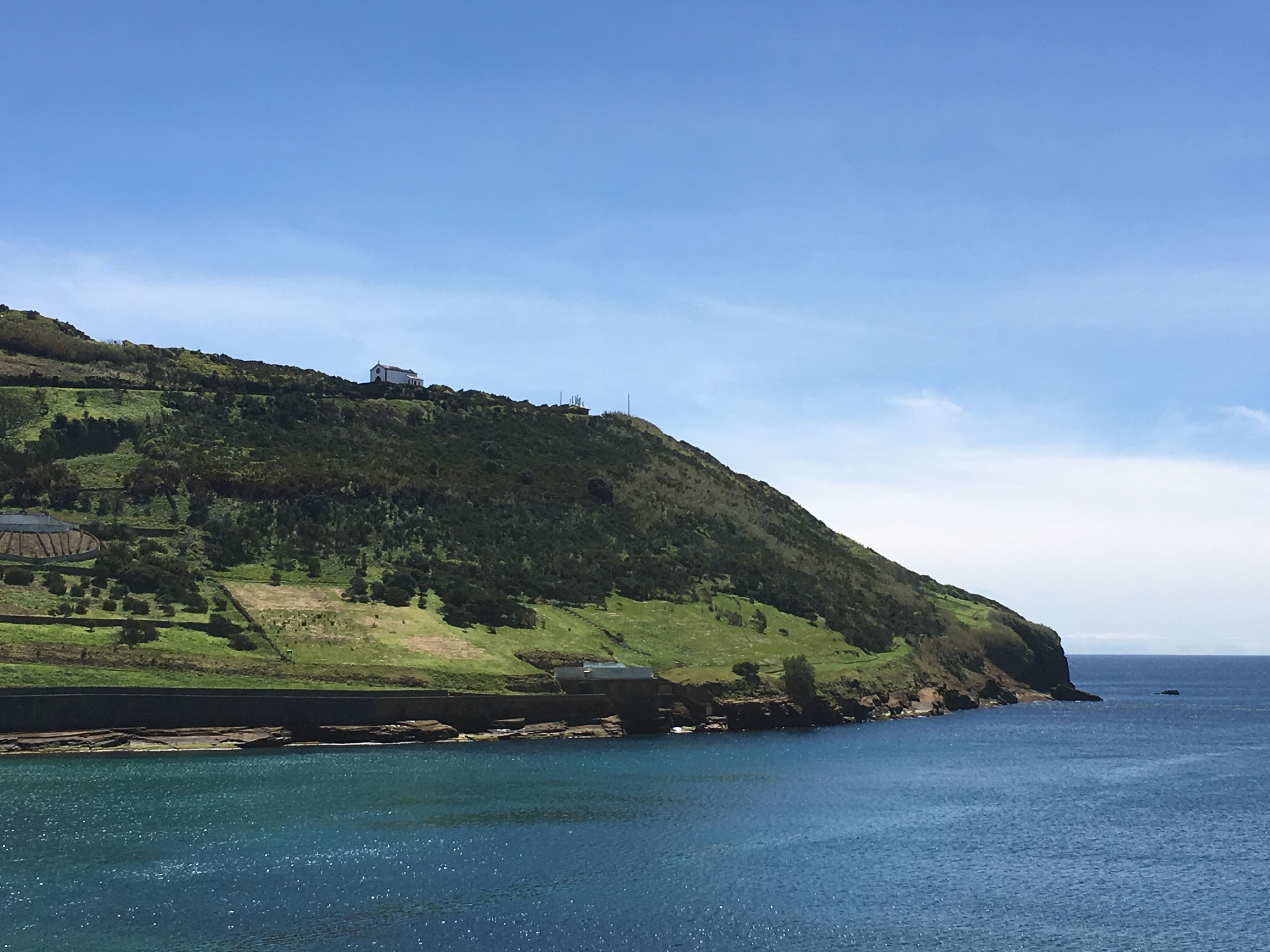 Un paysage côtier avec une colline, une petite maison au sommet et une étendue d’eau.