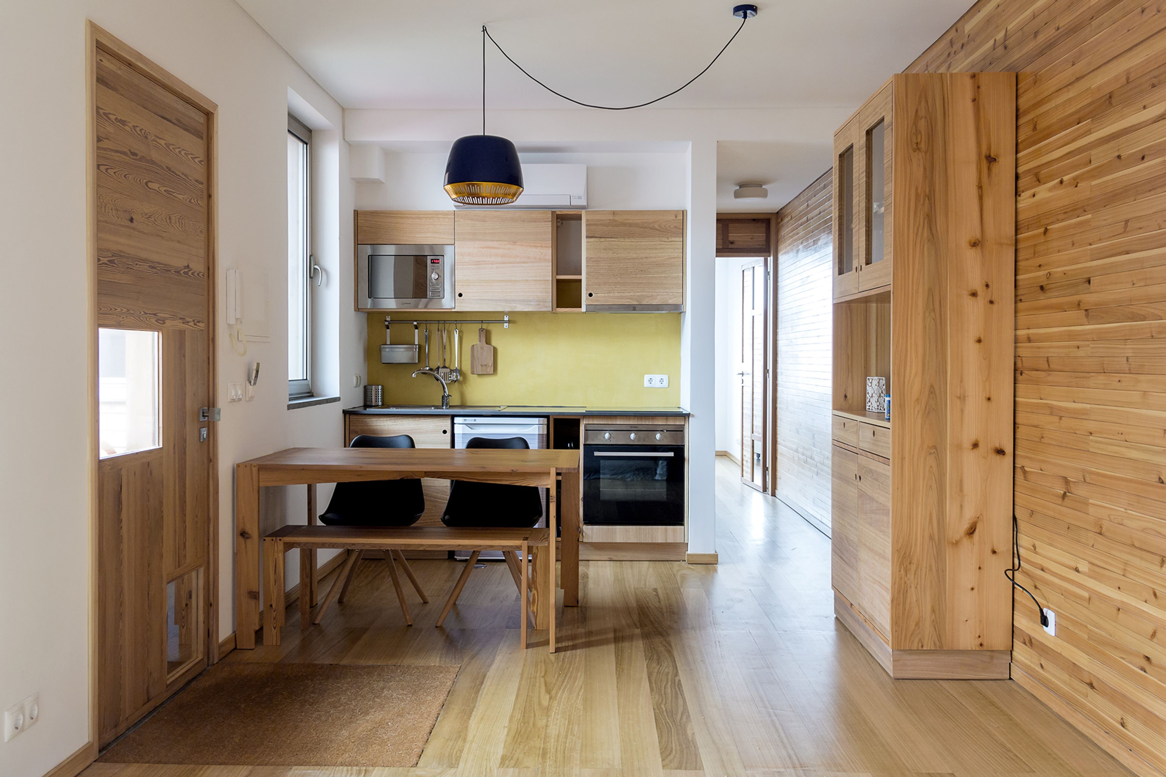 A modern kitchen with wooden cabinetry, a dining table, and a hanging light fixture.