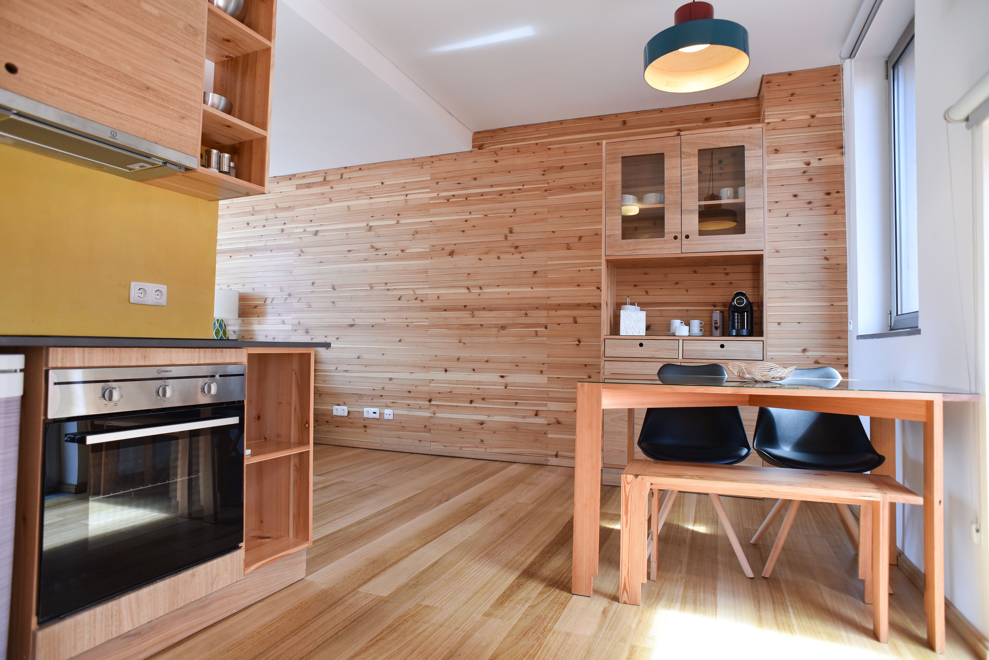 Une cuisine moderne avec des meubles en bois, un four encastré et un coin repas comprenant une banquette et des chaises.