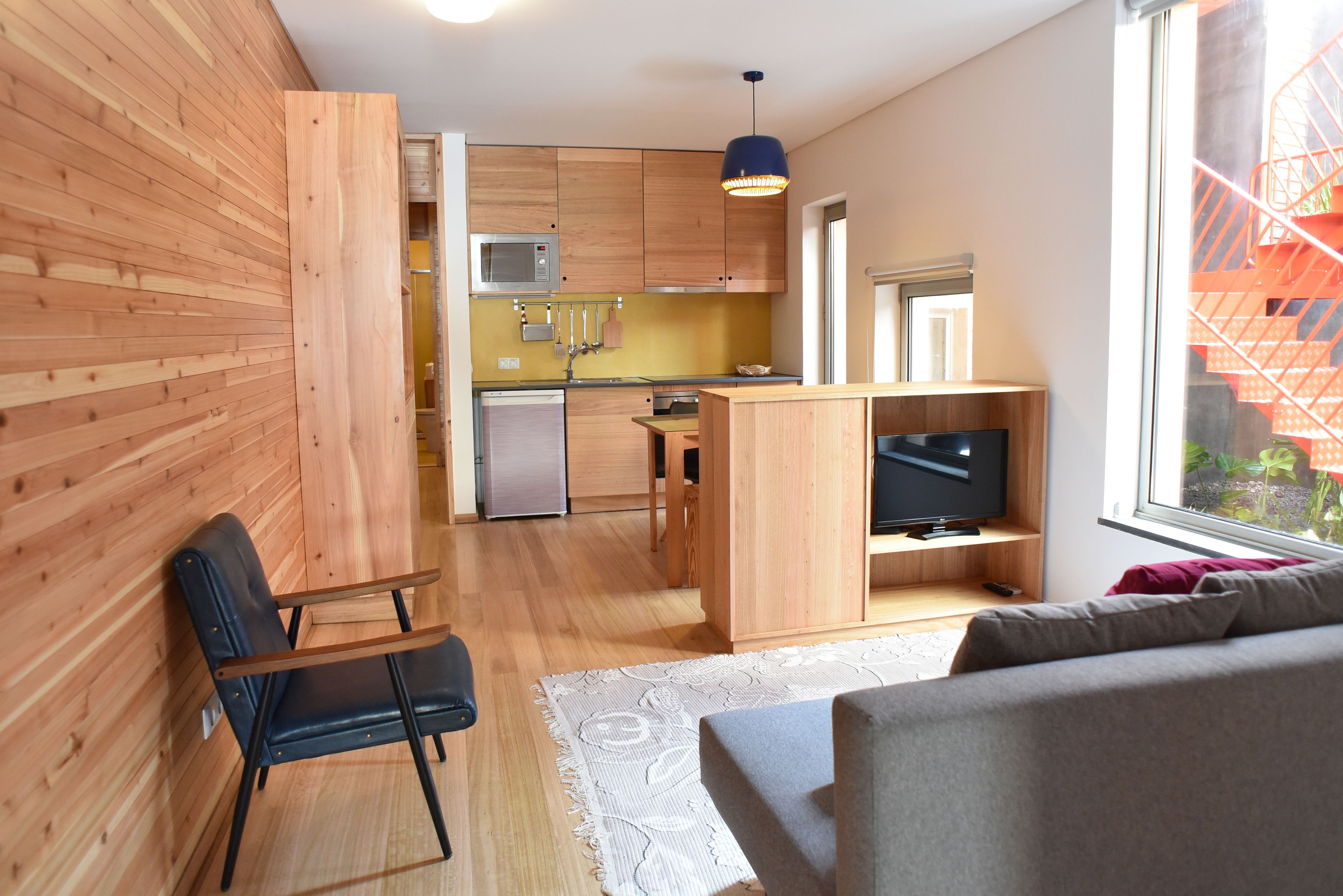 A modern apartment with wooden walls, a kitchenette, a dining area, a living room with a sofa, and a TV.