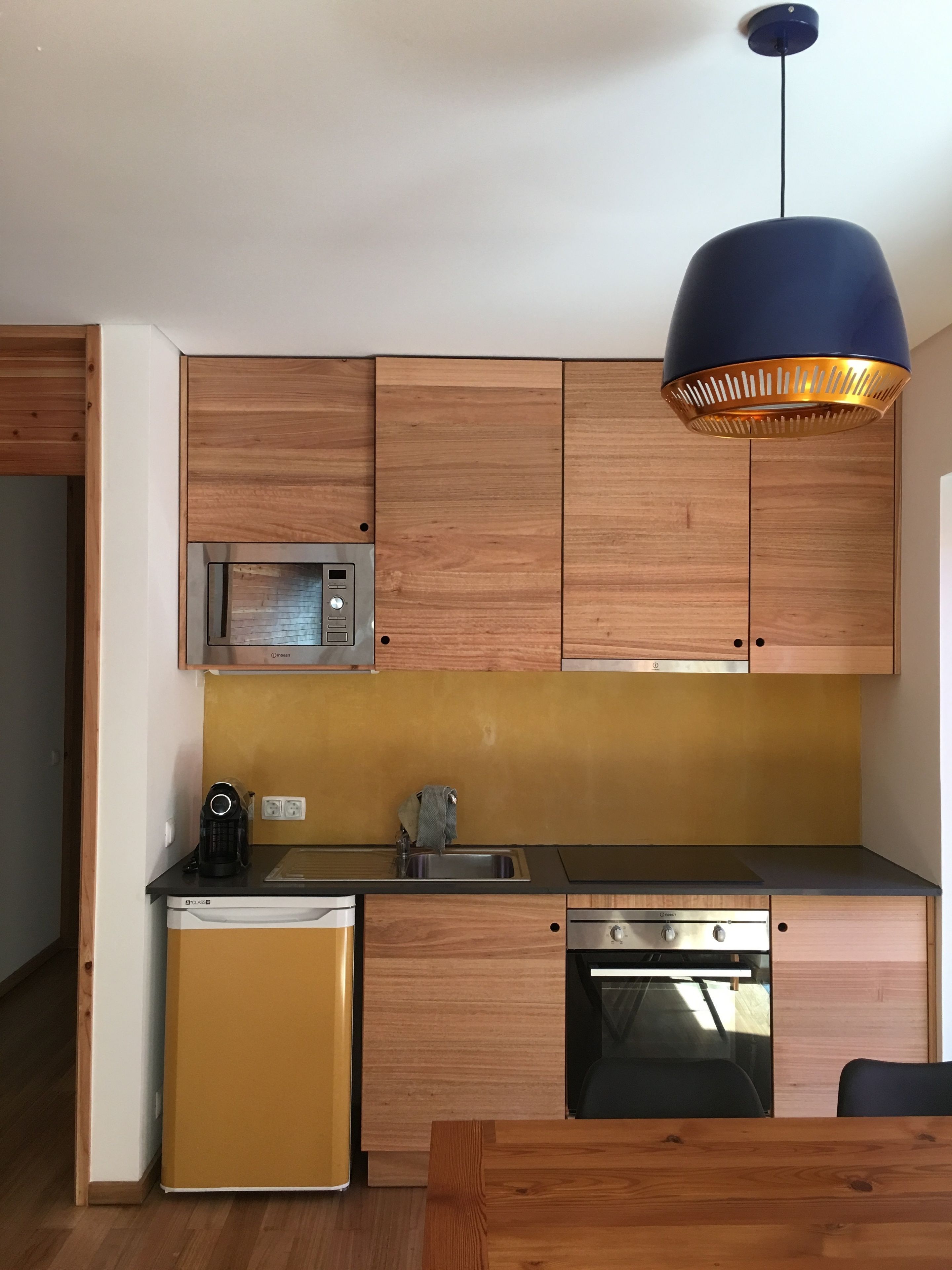 A compact kitchen with wooden cabinets, a built-in microwave, a sink, and a compact dishwasher.