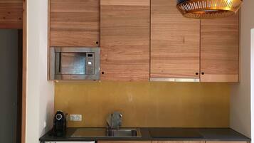 A compact kitchen with wooden cabinets, a built-in microwave, a sink, and a compact dishwasher.