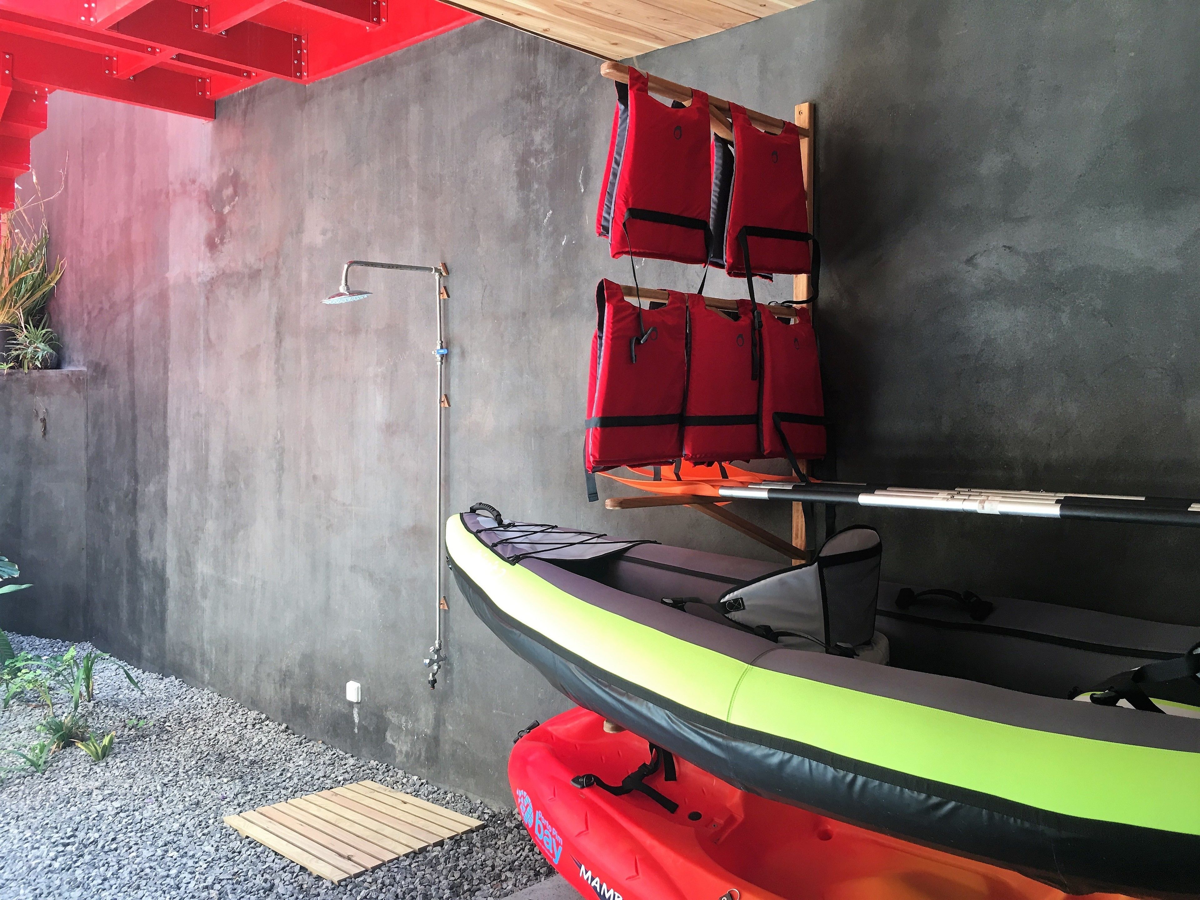 A kayak storage area with a concrete wall, a wooden deck, and red life jackets hanging on a rack.